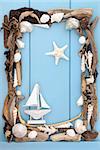Sea shell and driftwood with small decorative boat forming an abstract border over wooden blue background.
