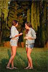 two teenage girls outdoors in jeans wear talking looking at each other