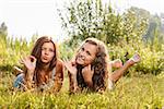 two girlfriends in T-shirts  lying down on grass showing ok sign looking at camera