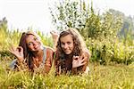 two girlfriends in T-shirts  lying down on grass showing ok sign looking at camera