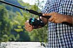 closeup of fisher on river with hands on reel, relaxing and fishing trout