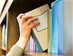 Hand pulling a book off the shelf. Blue colors books
