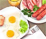 Breakfast - fried eggs, salad, bacon, sausages, bread and glass of orange juice.