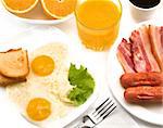 Breakfast - fried eggs, salad, bacon, sausages, bread, cut orange, glass of orange juice and cup of coffee.