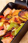 Homemade Salmon Stew with Potato, Red Bell Pepper, Leek and Carrot in Black Frying Pan closeup on Wooden background