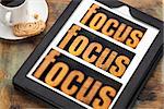 focus word in and out of focus  - text in vintage letterpress wood type on a digital tablet with a cup of coffee