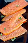 Slices of Delicious Smoked Salmon with Thyme closeup on Black Plate