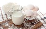 Baking ingredients with milk, eggs, whisk and flour on the table