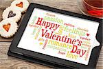 Happy Valentines Day word cloud on a digital tablet with heart cookies and a cup of tea