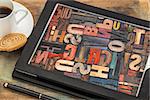 typography concept - alphabet abstract in vintage letterpress wood type on a digital tablet screen with a cup of coffee