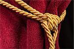Red velvet curtain with tassel. Close up knot on rope
