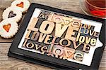 love word abstract - in vintage letterpress wood type printing blocks on a digital tablet with cup of tea and heart cookies