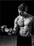 Photo of a man in his early thirties doing bicep curls with a dumbbell over a black background. Black and white version.