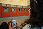Teenage girl sitting in laundromat, wearing headphones and using smart phone, Germany