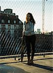 Teenage girl standing outdoors next to chain link fence near comercial dock, holding skateboard, Germany