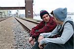 Two teenage boys sitting on railroad tracks together, near harbour, Germany
