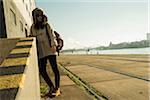 Teenage girl outdoors, wearing trapper hat and sunglasses, standing next to building at loading dock, Mannheim, Germany