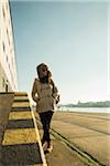 Teenage girl outdoors, wearing trapper hat andsunglasses, standing next to building at loading dock, Mannheim, Germany