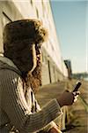 Close-up of teenage girl outdoors, wearing trapper hat and sunglasses, sitting next to building at loading dock, looking at smart phone, Mannheim, Germany