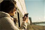 Close-up of teenage girl outdoors wearing sunglasses, sitting next to building at loading dock, looking at smart phone, Mannheim, Germany