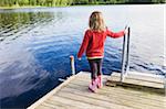 3 year old girl in red shirt on wooden dock looking at a lake, Sweden