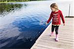 3 year old girl in red shirt on a pier holding a stick and playing in the water, Sweden