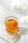 A small glass jar with clear golden honey and a honey comb with cotton swabs and cotton balls. High key image of honey and beauty products.