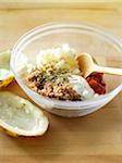 Bowl of mixture for making stuffed baked potatoes containing ground turkey, sour cream, rosemary, seasoning, salsa, and mashed potatoes. Two baked potato skins sit beside the bowl on a wooden cutting board