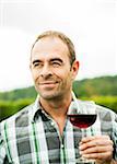 Portrait of vintner standing in vineyard, holding glass of wine, Rhineland-Palatinate, Germany