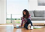 Teenage girl sitting on floor next to sofa, using laptop computer, Germany