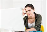 Teenager girl smiling, sitting in front of desktop computer monitor, studio shot
