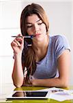 Young woman with pen and tablet computer, thinking and problem solving, studio shot