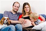 Happy young family sitting on the blue sofa expecting new baby