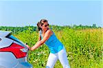 Young beautiful woman is pushing broken car on the road