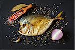 Smoked fish with spices and herbs on a black background.