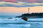 The iconic lighthouse of Biarritz, under a pinkish morning sky. Big waves hitting the rocks.