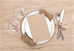 Blank paper on plate, wine glasses and silverware set on wooden table