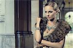 fashion portrait of luxury blond girl posing with elegant hair-style, fur shawl and precious shiny jewelery. Cute make-up