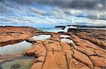 Ocean waves splash against spectacularrock formations at North Avoca, NSW Australia, with serene rockpools in the foreground.