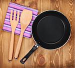 Frying pan and kitchen utensils on wooden table background. View from above