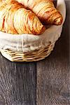 Fresh croissants in a basket on a wooden background with copy space.