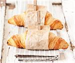 Fresh croissants wrapped in paper on an old white board.