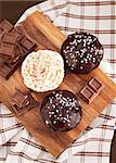 Chocolate cupcakes decorated with glaze and cream on wooden board