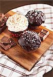 Chocolate cupcakes decorated with  glaze and cream on wooden board