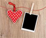 Blank instant photo and red heart hanging. On wooden background