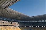 This is the modern stadium, seats are painted a yellow and a blue. The range of building colors blend well with blue sky.