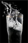 A cube of ice falling into a glass of water, beautiful splashes on black background.