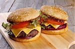 Tasty Hamburgers with Beef, Tomato, Lettuce, Pickle, Red Onion and Cheese into Sesame Buns closeup on Wooden Cutting Board