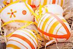 Close-up of decorative traditional Easter eggs, painted with yellow and orange horizontal stripes, with ribbons and straw, on a rustic wooden table