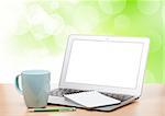 Laptop with blank screen and cup on table over sunny day background